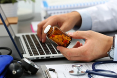 Image of doctor holding a prescription bottle while typing on a computer